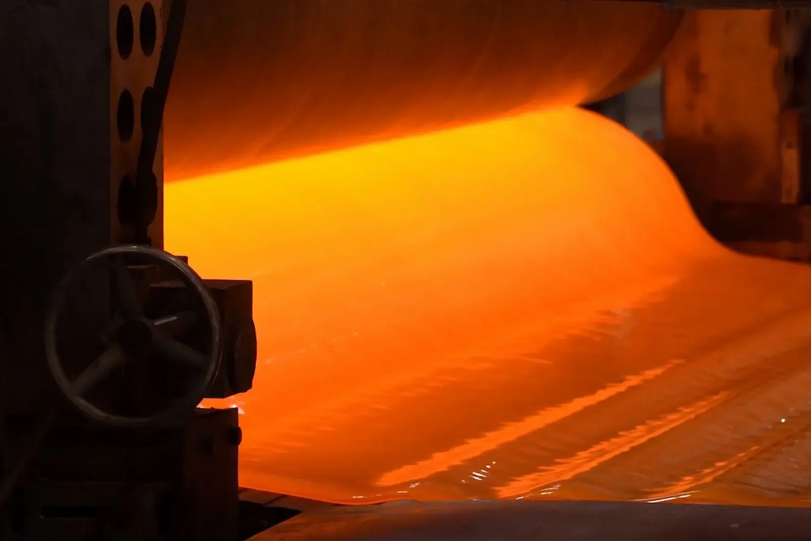 Glowing molten glass sheet passing between rollers on the production line